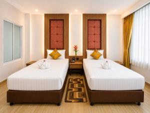 two beds in a room with white walls and wood floors at Aiyara Palace in North Pattaya