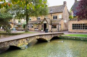 a bridge over a river in front of a building at Hideaway Cottage in Bourton on the Water