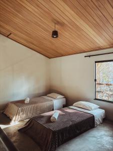 two beds in a room with a wooden ceiling at Girassóis do Vale - Chalés no Vale do Capão in Caeté-Açu