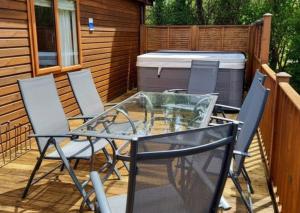 a glass table and chairs on a deck with a hot tub at Devon Comfort Lodge with Hot Tub - Spa Resort in Devon in Chudleigh