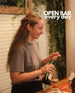 a woman holding a bottle of wine with the words open bar every day at Casa Caravan - Plant Based Concept House in Buenos Aires