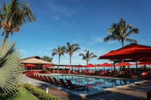 a swimming pool with red umbrellas and chairs and palm trees at Hotel Manati in Barra Grande