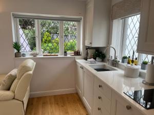 a kitchen with white cabinets and a sink and two windows at Garden Lodge, boutique - Walton on Thames in Walton-on-Thames