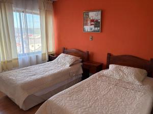 two beds in a room with orange walls and a window at Altos de Miramar in Puerto Montt +1 photo