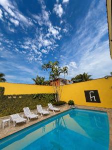 a swimming pool with chairs and a yellow wall at Pousada Cantinho do Mar - pé na areia in Guarujá