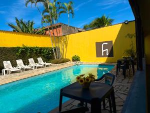 a pool with chairs and a table next to a yellow wall at Pousada Cantinho do Mar - pé na areia in Guarujá +7 photos