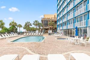a swimming pool with white chairs and a building at Penthouse 1BR + Bunk Room Boardwalk View Zone in Myrtle Beach