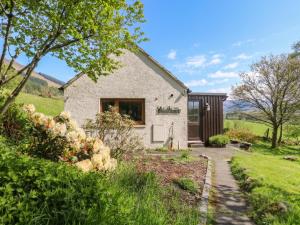 a stone cottage in a field with a pathway at Puidrac Cottage in Lochearnhead
