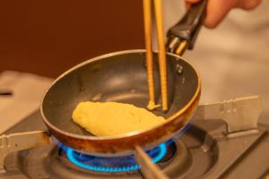 a person cooking food in a pan on a stove at Washu Blue Resort風籠 Kasago in Kurashiki