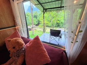 a teddy bear sitting on a bed in front of a window at Amornkeeree Khao Sok Camping in Khao Sok National Park