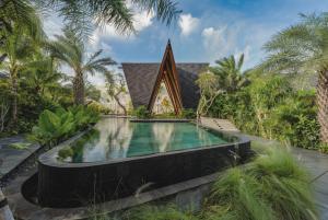 an infinity pool in front of a house with palm trees at Nuju Uluwatu - Adults Only in Uluwatu