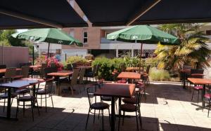 a group of tables and chairs with green umbrellas at Hôtel des Voyageurs in Changé