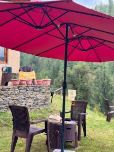 a red umbrella over a table and two chairs at Shikhar cottage in Jibhi