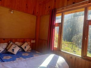 a bed in a room with a large window at Shikhar cottage in Jibhi
