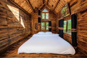 a bed in a room with wooden walls and windows at Sóc House Măng Đen in Kon Plong
