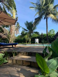 a pool with palm trees and a bench and an umbrella at Beach House - private room in Diani Beach