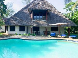 a house with a thatched roof and a swimming pool at Beach House - private room in Diani Beach