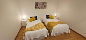 two beds in a room with white walls and yellow pillows at Casa dos Azevedos in Câmara de Lobos
