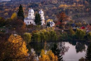 a church sitting on top of a hill next to a lake at La tataie Nucșoara in Nucşoara