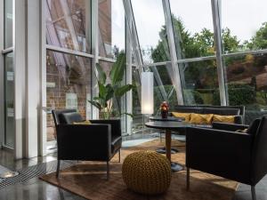 a living room with a table and chairs and large windows at Mövenpick Hotel Münster am Aasee in Münster