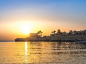 a sunset over a body of water with palm trees at Movenpick Resort El Quseir in Quseir