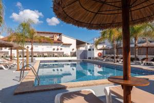 a swimming pool with an umbrella and chairs at Hotel Chevy & Suites in Cala Ratjada