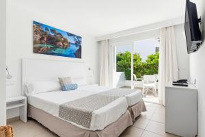 a white bedroom with a bed and a window at Hotel Chevy & Suites in Cala Ratjada