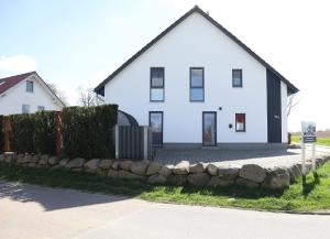 a white house with a stone wall in front of it at Design-FeWo Fleesensee, Wallbox, Sauna, Terrasse in Unter Göhren