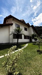 a large white house with a palm tree in the yard at Refúgio na Serra - natureza e conforto in Teresópolis