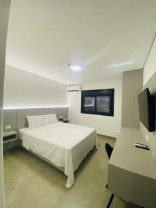 a bedroom with a white bed and a flat screen tv at Hotel Morada do Sol in Chavantina