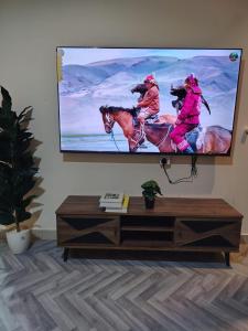a flat screen tv on a wall with two people riding horses at Sukoon Apartment شقة سكون 2 in Buraydah +8 photos
