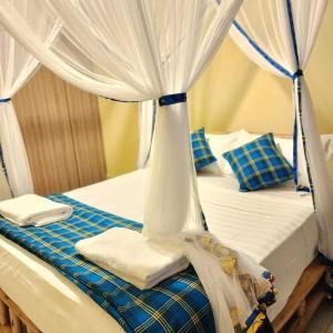 a canopy bed with white curtains and blue sheets at M- NET LUXURIOUS HOTEL KAGADi in Kagadi