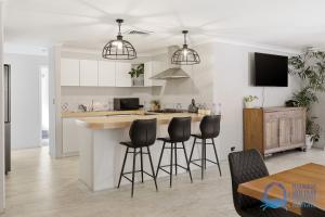 a kitchen with a bar with four stools in it at Mandurah Poolside Retreat in Coodanup