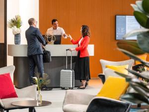 a man and a woman standing at a counter in an office at Mercure Geneva Airport in Geneva