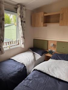 two beds in a small room with a window at 10 the green lilliardsedge carvan park harritsfield jedbrugh td8 6tz in Harrietsfield