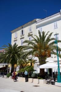 a large white building with palm trees in front of it at Ridzak Riva Rooms in Mali Lošinj