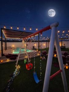 a swing on a patio at night with the moon at شاليه غرام حتا - Hatta Romance Chalet in Būbādī +5 photos