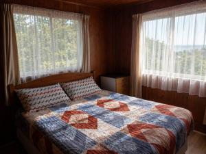 a bedroom with a bed with a quilt and two windows at El Urco Chiloé - Cabaña Guapilacuy in Ancud