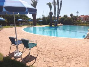 two chairs and an umbrella next to a swimming pool at Villa comfort in Bouznika