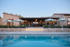 a pool with chairs and umbrellas next to a building at Hotel Rural Es Riquers in Porreres