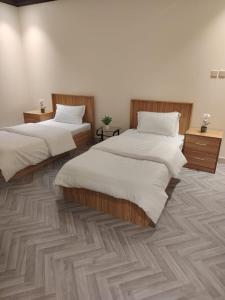 two beds in a room with wooden floors at Sukoon Apartment شقة سكون 2 in Buraydah