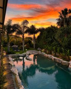 a pool in a yard with palm trees and a sunset at Residence Villa Rosa dei Venti in Cinisi