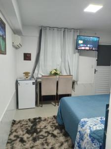 a room with a bed and a table and a television at QUARTO AZUL com cozinha e piscina só sua in Capão da Canoa