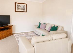 a living room with a white couch and a television at Palmers Lane Vineyard Cottage in Pokolbin