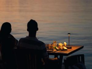 a man and a woman sitting at a table near the water at V Villas Maldives at Mirihi - MGallery Collection in Mandhoo