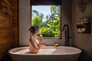 a woman sitting in a bath tub looking out a window at Edge of Ubud by GenuineHost in Ubud +100 photos