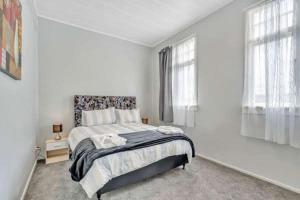 a white bedroom with a bed and two windows at Ruawai Post Office Accommodation in Ruawai