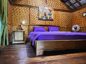 a bedroom with a bed with purple sheets and a painting at Jonny's Places in Tetebatu