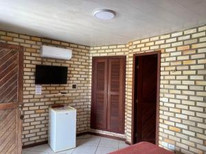 a room with a brick wall with a television and a refrigerator at Pousada Chalés do Cunhaú in Canguaretama