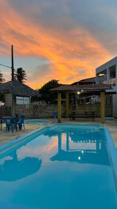 a blue swimming pool with a sunset in the background at Pousada Chalés do Cunhaú in Canguaretama